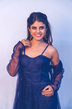 a woman in a blue dress posing for the camera with her hand on her shoulder