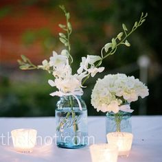 two mason jars filled with white flowers and lit candles