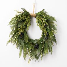 a christmas wreath hanging on the wall with greenery and berries around it, decorated with twine