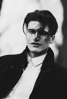 black and white photograph of a man with long hair wearing a coat, shirt and tie