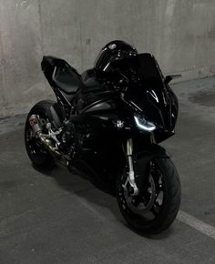 a black motorcycle is parked in a parking lot next to a concrete wall and cement floor