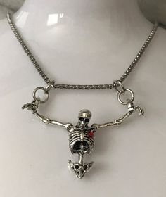 Embrace the darker side of fashion with our Hanging Skeleton Torso Necklace on a stainless steel 18" chain. This unique piece features a silver skeleton hanging from both wrists, adding a touch of Gothic flair to any outfit. You have the option to personalize your necklace by choosing between a skeleton with or without a striking red rhinestone heart accent. The skeleton's head is elegantly tilted forward, enhancing its macabre charm. Perfect for Halloween or as a statement accessory, this necklace comes beautifully presented in a sleek black gift box, making it an ideal gift for those who appreciate edgy and distinctive jewelry pieces. Halloween Metal Necklace With Adjustable Chain, Nickel-free Metal Necklace For Halloween, Edgy Necklace For Halloween Gift, Punk Necklace With Lobster Clasp As Gift, Halloween Emo Chain Jewelry, Heart-shaped Metal Jewelry For Halloween, Emo Halloween Chain Jewelry, Halloween Emo Style Chain Jewelry, Edgy Halloween Necklace Gift