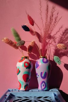 two colorful vases sitting on top of a blue table next to a pink wall