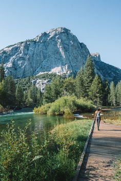 a person walking across a wooden bridge over a river next to a large mountain range