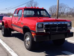 a red pick up truck is parked on the side of the road in front of another truck