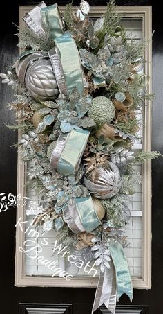 a christmas wreath hanging on the side of a door with blue ribbons and ornaments around it