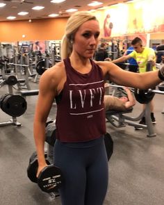 a woman in a gym with dumbs on her arm and another person behind her