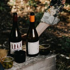 two bottles of wine sitting on top of a wooden table next to glasses and olives