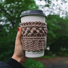 a hand holding a coffee cup with a crochet pattern on the sleeve and lid