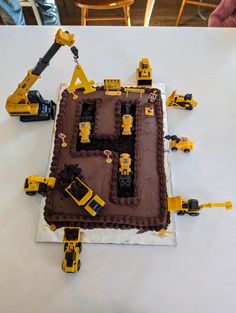 a chocolate cake with construction vehicles on it sitting on top of a white tablecloth