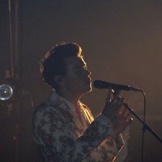 a man standing in front of a microphone on top of a stage with lights behind him