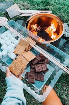 a person sitting in front of a fire with marshmallows and crackers