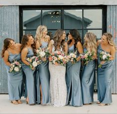 a group of women standing next to each other in front of a building holding bouquets