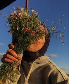 a woman holding flowers up to her face with the sky in the back ground behind her