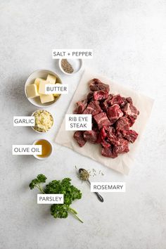 ingredients to make beef stew laid out on a cutting board, including parsley, salt, pepper, butter, garlic, and oil