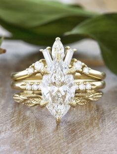 a pear shaped diamond ring set on top of a wooden surface with leaves in the background