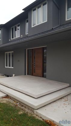 an empty concrete patio in front of a large gray house with two doors and windows