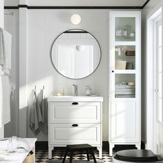 a white bathroom with black and white checkered flooring, round mirror above the sink