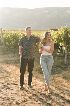 a man and woman walking in the middle of an open field with vines behind them