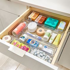 an open drawer with various items in it on the floor and white counter top,