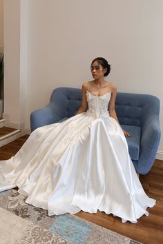 a woman is sitting on a couch in a white dress and posing for the camera