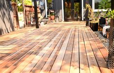 a wooden deck in front of a house with potted plants on the other side