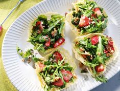 four tortillas with strawberries, lettuce and other toppings on a paper plate