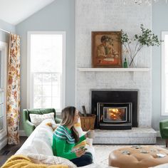 a woman sitting on a couch reading a book in front of a fire place that is built into the wall