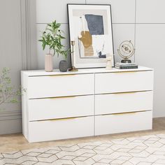 a white dresser with gold handles and drawers in front of a painting on the wall