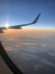 the wing of an airplane as it flies through the sky with clouds and sun in the background