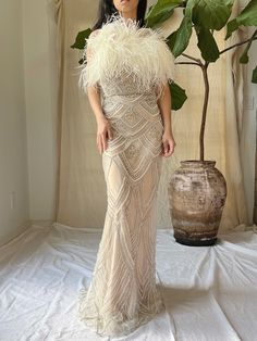 a woman standing in front of a potted plant wearing a dress with feathers on it