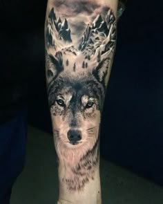 a man's arm with a wolf tattoo on it and mountains in the background