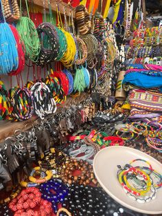 many bracelets and necklaces are on display in a market stall, including one with a white plate