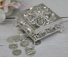 a small silver box sitting on top of a white table next to some coins and flowers