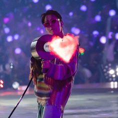 a woman holding a heart shaped object while standing on top of a street at night