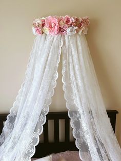 a canopy bed with pink flowers on the top and white netting over it, in front of a beige wall