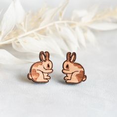 two wooden rabbits sitting next to each other on top of a white surface with feathers in the background