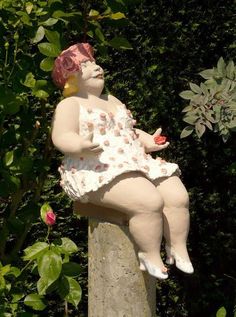 a statue of a woman sitting on top of a cement pillar in front of trees