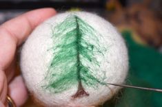 a person is holding a needle with a small felt tree on it