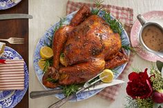 a roasted turkey on a blue and white plate next to a cup of coffee, silverware, and flowers