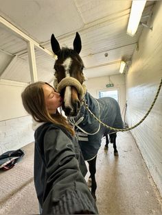 a woman kissing a horse wearing a blanket on it's head in an enclosed area