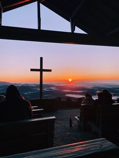 people sitting on benches at the top of a hill watching the sun rise over mountains