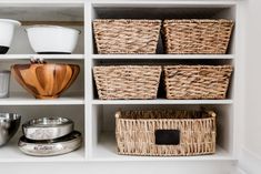 wicker baskets and bowls sit on shelves in a kitchen cupboard with white walls behind them