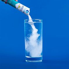 a person pouring something into a glass filled with water on a bright blue background,