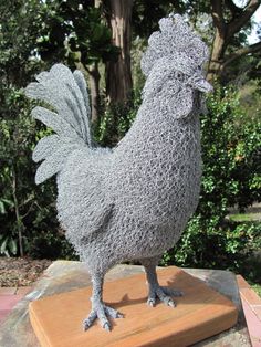 a statue of a chicken on top of a wooden block in front of some trees