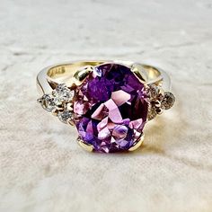 A stunning 14 karat yellow gold cocktail ring set with an oval amethyst weighing approximately 2 carat. Amethyst is the birthstone for February. It is shouldered by 6 round diamonds weighing approximately 0.20 carat (G-H SI1-I1). This ring is a size 4.75 US / J UK. > Resizing not included. This ring can be resized to fit most fingers. Please contact us for details. Resized rings are final sale. It weighs 3 grams. Birthstone: February/April. Condition: Very Good. Faint scratches throughout metal. Oval Amethyst Ring With Diamond Accents For Anniversary, Oval Amethyst Ring With Accent Stones For Anniversary, Anniversary Oval Amethyst Ring With Diamond Accents, Classic Oval Amethyst Ring With Accent Stones, Elegant Oval Multi-stone Amethyst Ring, Oval Amethyst Ring With Gemstone Accents, Oval Amethyst Ring With Diamond Accents In Yellow Gold, Oval Amethyst Ring With Diamond Accents, Oval Amethyst Ring In Yellow Gold With Diamond Accents