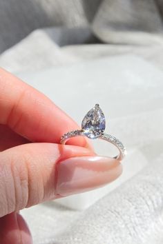 a woman's hand holding an engagement ring with a pear shaped diamond on it