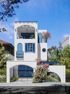 a large white house with blue windows and balconies on the second floor is surrounded by greenery