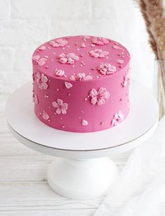 a pink cake with flowers on it sitting on top of a white plate next to a vase