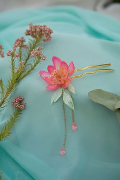 a pink flower is laying on top of a blue cloth with greenery and flowers